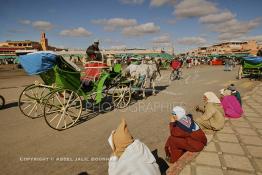 Image du Maroc Professionnelle de  S'asseoir au bord des trottoirs fait partie des habitudes pour certaines personnes d'une époque presque révolue au Maroc, cela perdure encore dans quelques région lointaines surtout pour les personnes âgées. Sur la mythique place Jemaa El Fana de Marrakech, presque vide durant la période où le soleil est au zénith, le cocher fixe le grand père à gauche pour le transporter dans sa calèche avec sa famille, puisque c'est évident qu'ils ne sont pas des résidents de la ville touristique du Maroc, le 2 Mars 2004. (Photo / Abdeljalil Bounhar) 